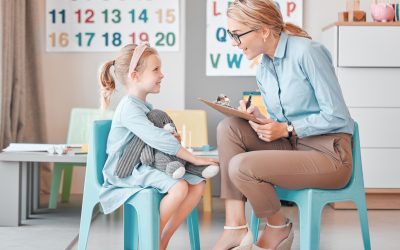 Young smiling caucasian child psychologist sitting with an adorable little girl in a clinic and using a clipboard for a consult. Cute girl talking to a mental health professional. Dyslexia and anxiety Young smiling caucasian child psychologist sitting with an adorable little girl in a clinic and using a clipboard for a consult. Cute girl talking to a mental health professional. Dyslexia and anxiety